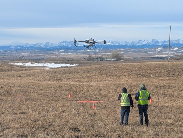 Two drone pilots stand in the distance wearing high vis PPE facing a large agricultural spray drone