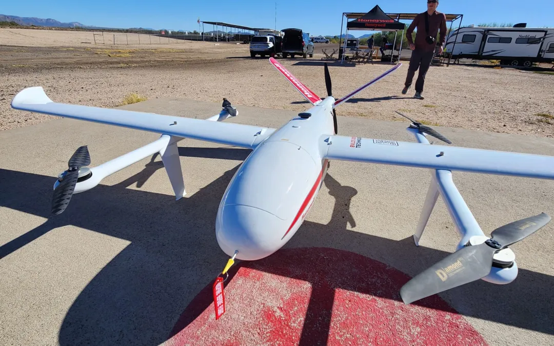 Two drone pilots stand in the distance wearing high vis PPE facing a large agricultural spray drone